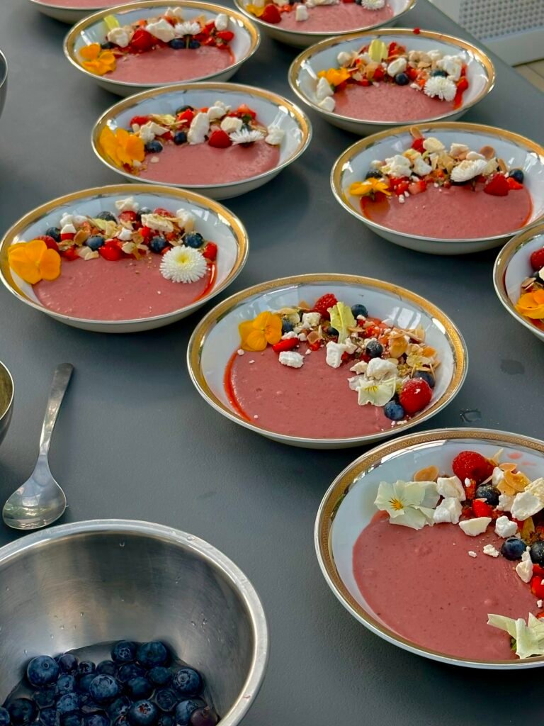 Rožinės spalvos uogų putėsiai (smoothie bowl) lėkštėse, papuošti šviežiomis uogomis, morengais ir valgomomis gėlėmis – Skonio šaukštelis receptai.