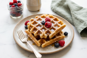 Auksinės spalvos traškūs vafliai su šviežiomis uogomis ir klevų sirupu lėkštėje - geriausias vaflių receptas namuose
